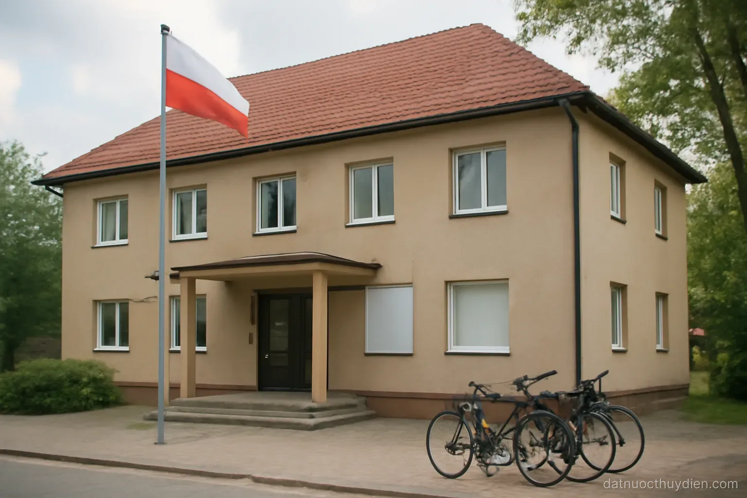 A small municipal building with a flagpole and parked bicycles outside, no readable text